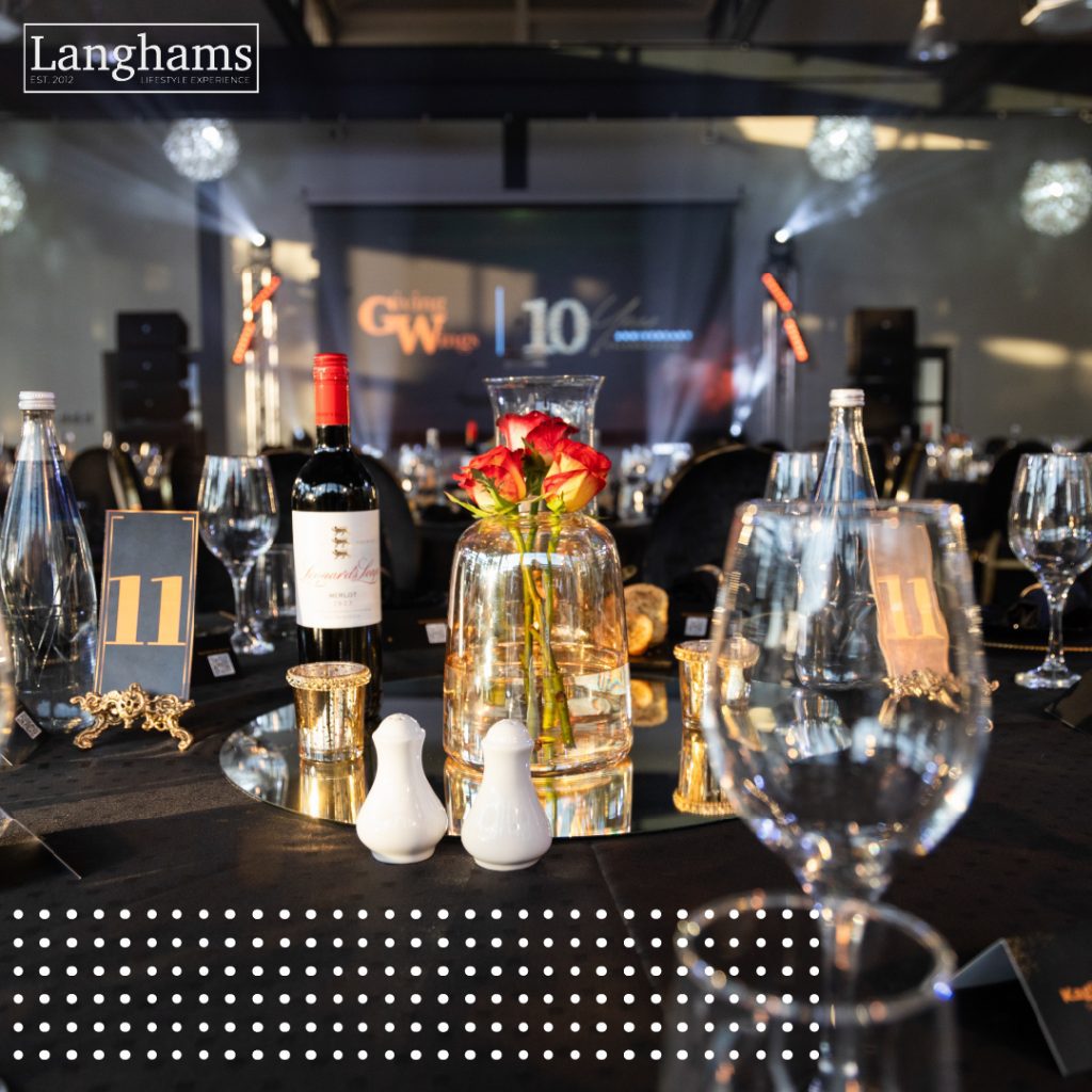 Elegant indoor event setup at Langhams with black table settings, wine, glassware, and a floral centerpiece, prepared for a formal year-end celebration.
