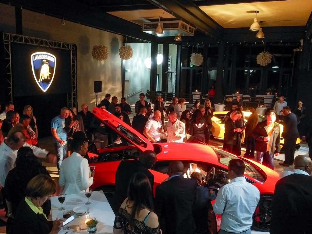 uests gathered at Langhams Lifestyle Estate for a Lamborghini launch event, featuring red and yellow supercars on display with the Lamborghini logo illuminated on a large screen.