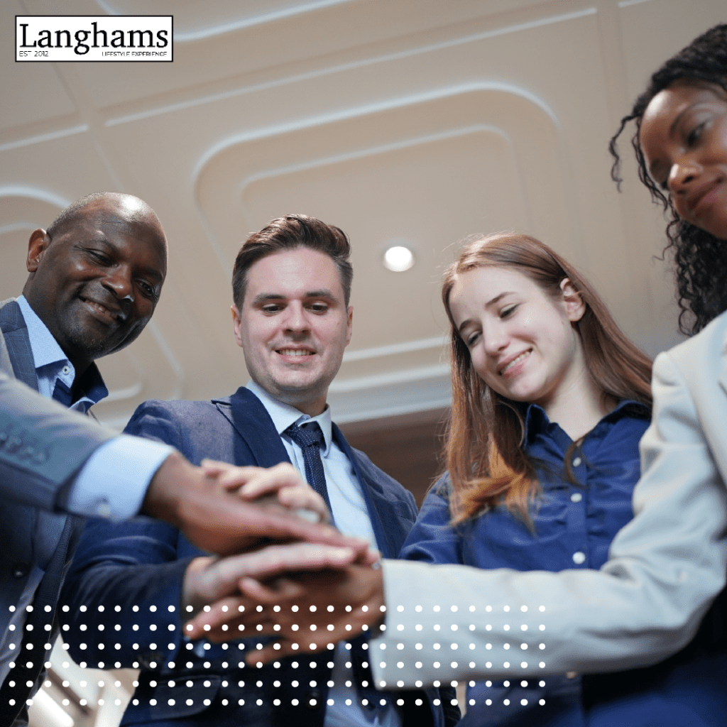 Diverse group of professionals joining hands in teamwork during a corporate event at Langhams Lifestyle Experience.